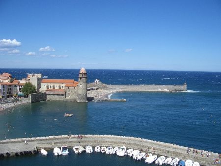 Collioure vue d'en haut : l'église et son clocher-phare au bord de l'eau, les remparts, la jetée et les barques