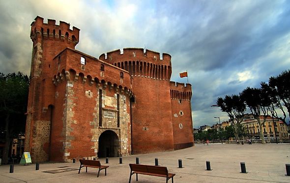 Le Castillet, porte fortifiée de brique rouge à créneaux de Perpignan, sous un ciel d'orage