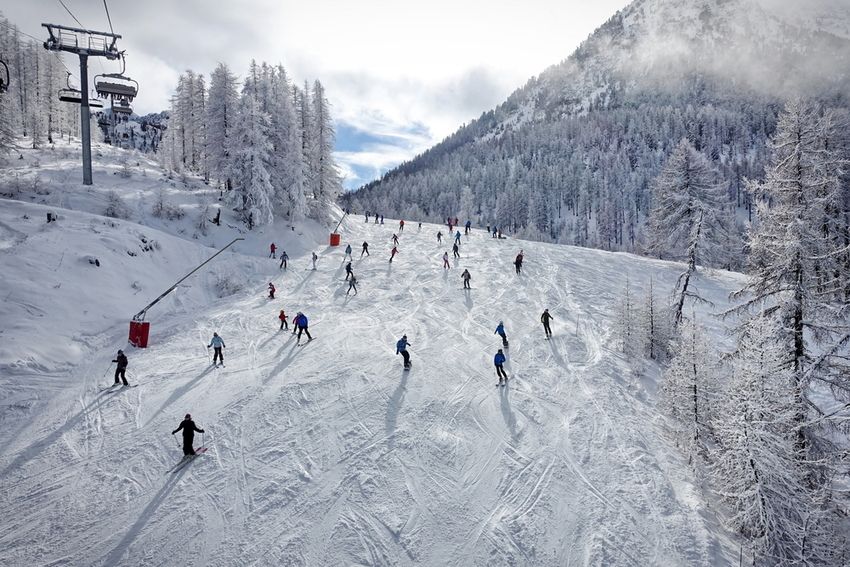 Skieurs sur une large piste bordée de mélèzes givrés à Montgenèvre, télésiège sur la gauche