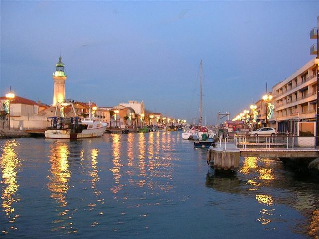 Le chenal du Grau-du-Roi à la tombée de la nuit : l'ancien phare, un chalutier amarré, les quais illuminés et leurs reflets dans l'eau
