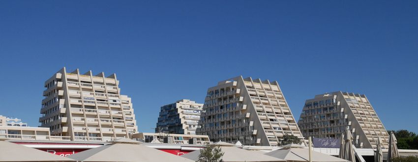 Les immeubles en forme de pyramide de La Grande-Motte sous un ciel bleu, derrière les parasols d'une terrasse