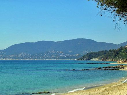 Une plage de sable et de rochers à La Croix-Valmer, eau turquoise et collines des Maures au fond