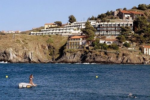 Une baigneuse sur un ponton flottant devant les rochers et les maisons accrochées au-dessus de la mer, sur la Côte Vermeille
