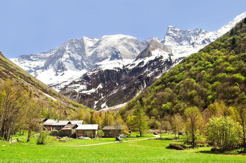 Vallée d'alpage verdoyante et hameau de chalets au pied des sommets enneigés de la Vanoise, en été