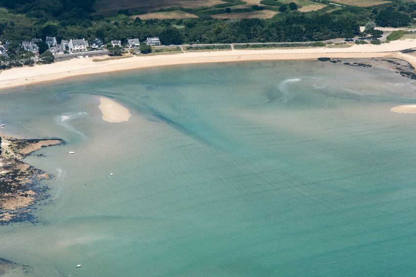 Vue aérienne d'une anse de sable de la côte morbihannaise à marée basse, avec bancs de sable, eau turquoise et maisons en bordure de plage