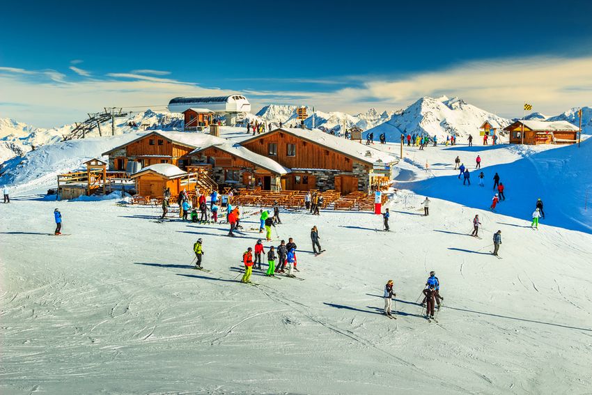 Skieurs devant un restaurant d'altitude en bois, au sommet des pistes des Menuires