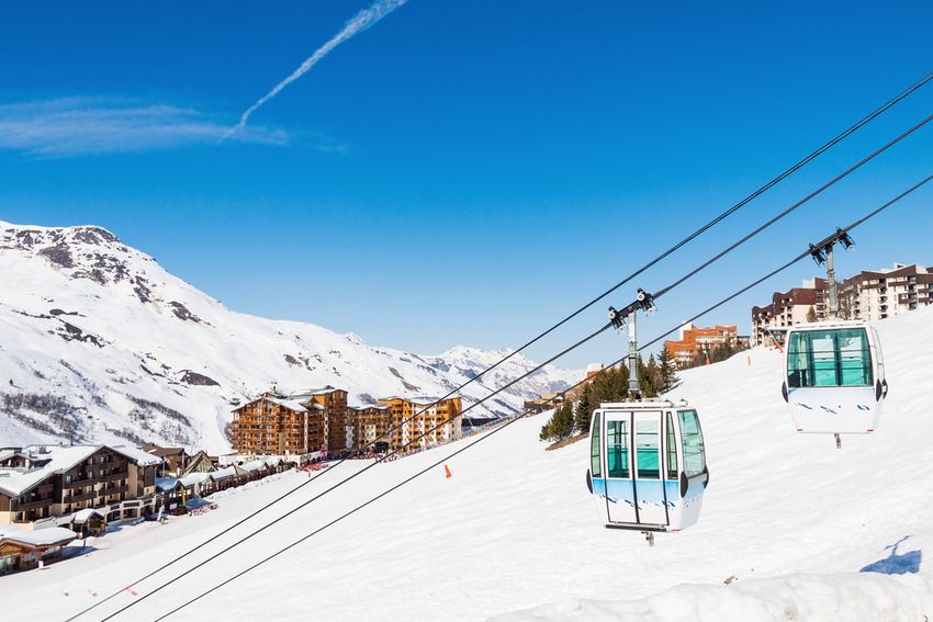 Deux cabines d'une télécabine au-dessus des résidences des Menuires, sous un ciel bleu