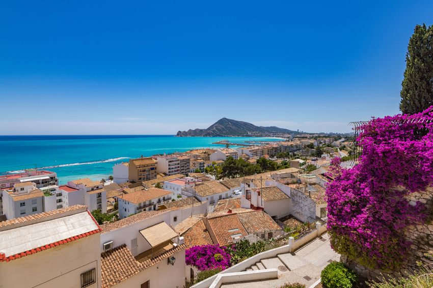 Les toits d'Altea et la baie turquoise jusqu'à la Serra Gelada, avec des bougainvilliers au premier plan