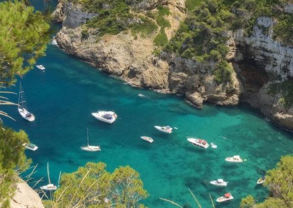 Bateaux de plaisance ancrés dans une crique d'eau turquoise bordée de falaises boisées, à Jávea