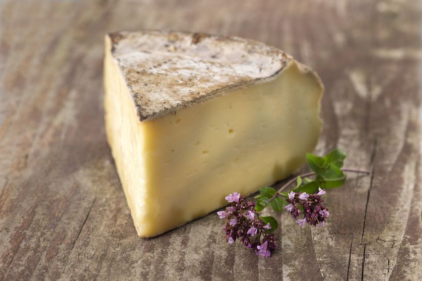 Un quart de tomme de Savoie à la croûte grise sur une planche de bois, avec un brin de thym en fleur