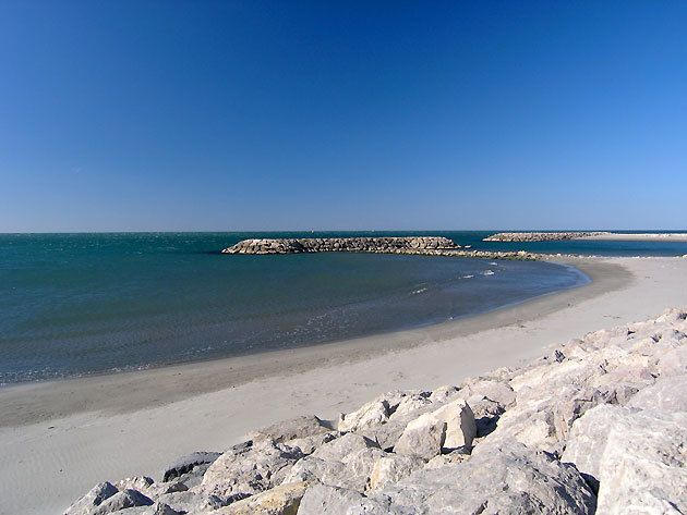 Une plage de sable clair au bord d'une eau calme, protégée par des digues de pierre, aux Saintes-Maries-de-la-Mer